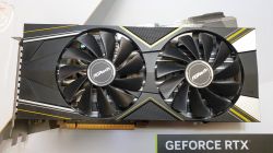 Karta graficzna ASRock z dwoma wentylatorami na białym tle, z elementami w żółto-szare paski