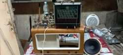Rozebrane radio lampowe na stole warsztatowym; obok głośnik i narzędzia, a skala radia stoi na obudowie.