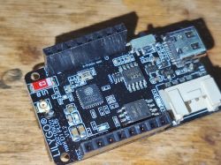 LilyGO D1 Mini Plus module with ESP32-C3 chip on a wooden background