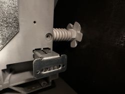 Zbliżenie na boczny element zmywarki z metalowym uchwytem i białą śrubą regulacyjną