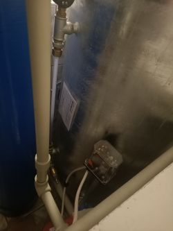 Zbliżenie na instalację wodną z widocznym manometrem i rurami przy zbiorniku.