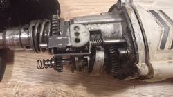Zbliżenie na otwartą obudowę mechanizmu młotowiertarki, widoczne koła zębate i sprężyny.