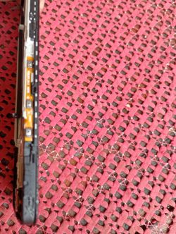 Boczna krawędź telefonu z taśmą flex przycisków w ramce, na tle różowej plecionki