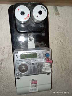 Licznik energii elektrycznej z bezpiecznikami i plombami zamontowany na ścianie.