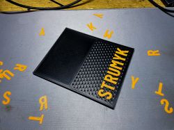Black case with yellow STRUMYK lettering on a gray mat with scattered letters around