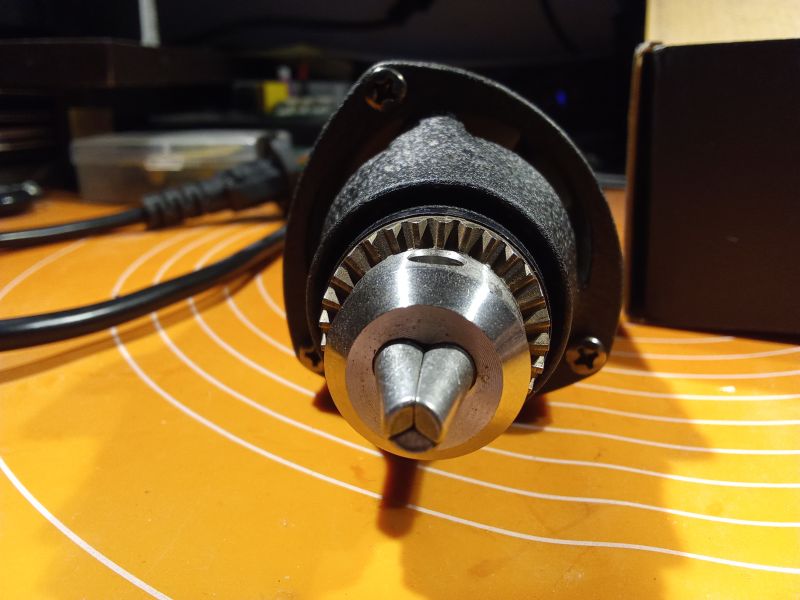 Zbliżenie na uchwyt wiertarski szlifierki na biurku z pomarańczową matą.