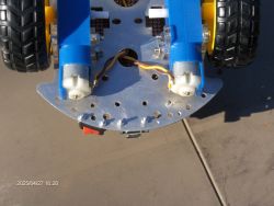 Close-up of a robot chassis with a metal base, black-and-yellow wheels, and two motors with visible white axles.
