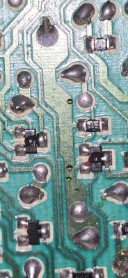 Zbliżenie na uszkodzone elementy SMD na zielonej płytce PCB.