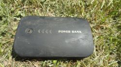 Czarny powerbank z napisem „POWER BANK” leżący na trawie