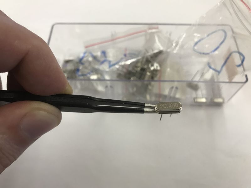 20 MHz quartz resonator held with tweezers, background box with other components