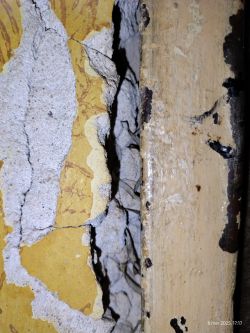 Zbliżenie na starą, uszkodzoną ścianę z widocznymi warstwami tynku i farby.