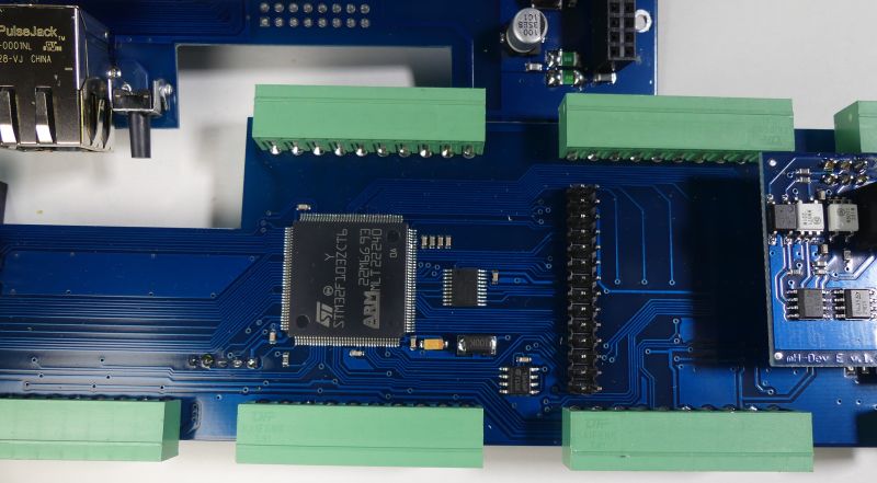 Zbliżenie na niebieską płytkę PCB z mikrokontrolerem STM32 i zielonymi złączami śrubowymi