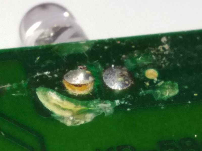 Zbliżenie na uszkodzoną płytkę drukowaną pilota z widocznymi uszkodzeniami i zabrudzeniami.