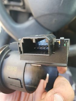 Zbliżenie na element elektroniczny w samochodzie, prawdopodobnie kondensator lub złącze, trzymany w ręce.