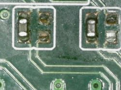 Zbliżenie płytki PCB z dwoma miejscami na elementy SMD; jedno wygląda na puste lub uszkodzone
