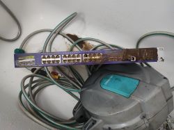 A mud-coated Extreme Networks Summit 300-24 network switch with cables in the background.