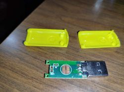 Zdjęcie otwartego urządzenia USB z pustą płytą PCB i żółtą obudową.