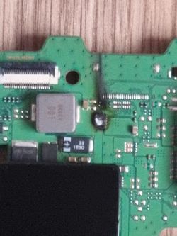 Zbliżenie na zieloną płytę PCB z gniazdem taśmowym, ekranem metalowym i czarną kroplą kleju