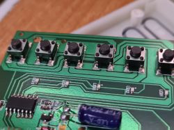 Zbliżenie na płytkę drukowaną z kilkoma przyciskami i elementami elektronicznymi.