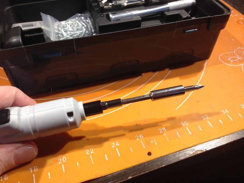 Elektryczny wkrętak z założonym bitem na tle skrzynki z akcesoriami.