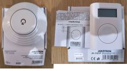 Dwa urządzenia Jablotron w pudełkach: czujka JA-111ST-A i termostat JA-110TP na drewnianym blacie