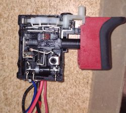 Rozłożony przełącznik wkrętarki z widocznymi wewnętrznymi elementami i okablowaniem.