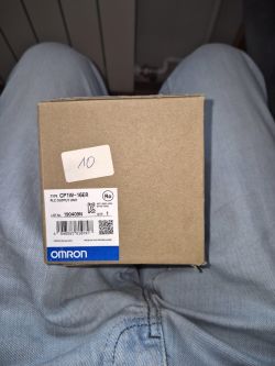 Pudełko Omron CP1W-16ER z etykietą produktu, trzymane na kolanach w dżinsach.