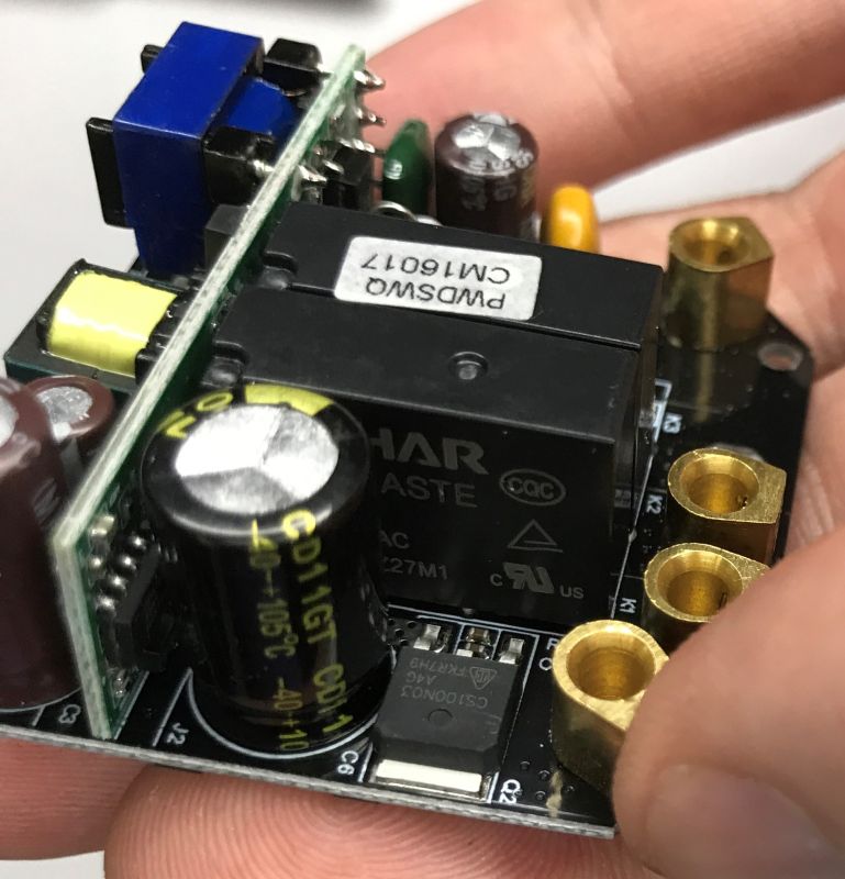 Close-up of a PCB with a relay, capacitors, and brass screw terminals, held in a hand