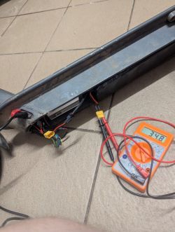 Otwarte wnętrze hulajnogi elektrycznej z widocznymi przewodami i miernikiem napięcia wskazującym 34.8.