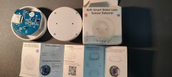 Tuya Wi-Fi Water Leak Sensor - Package Contents and Manuals Photo of a Tuya brand Wi-Fi water leak sensor with its case removed and user manuals.