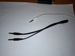 Zdjęcie adaptera audio z dwoma wtyczkami i jednym gniazdem na białym tle.