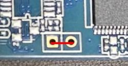 Close-up of a circuit board with a red wire bridge connecting two solder points.