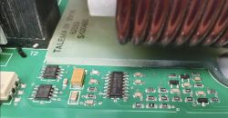 Zbliżenie płytki PCB z układem scalonym i komponentami SMD obok cewki.