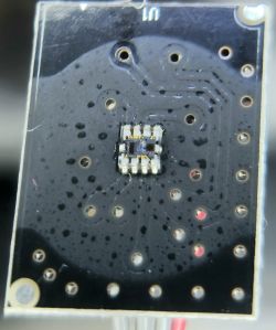 Zbliżenie płytki PCB z małym układem SMD na środku; na górze widoczny napis „Lm”.