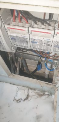 Skrzynka elektryczna z bezpiecznikami i kablami, w otoczeniu śniegu.