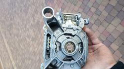 Silnik elektryczny z widocznymi szczotkami trzymany w ręku, na tle kostki brukowej.
