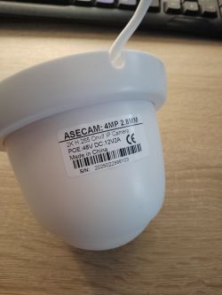 Kamera IP Asecam 4MP 2.8 mm trzymana nad biurkiem z widoczną etykietą techniczną