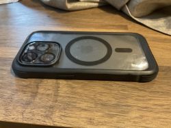 Smartfon w czarnym, pancernym etui leży obiektywem do góry na drewnianym blacie.