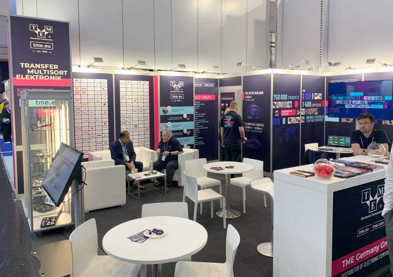 Stoisko TME na targach embedded world 2024 z siedzącymi osobami oraz materiałami promocyjnymi.