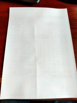 Arkusz papieru z pionowym zagięciem pośrodku, leżący na brązowym biurku.