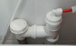 Zbliżenie na biały plastikowy odpływ z podłączonym czerwonym wężykiem 6 mm.