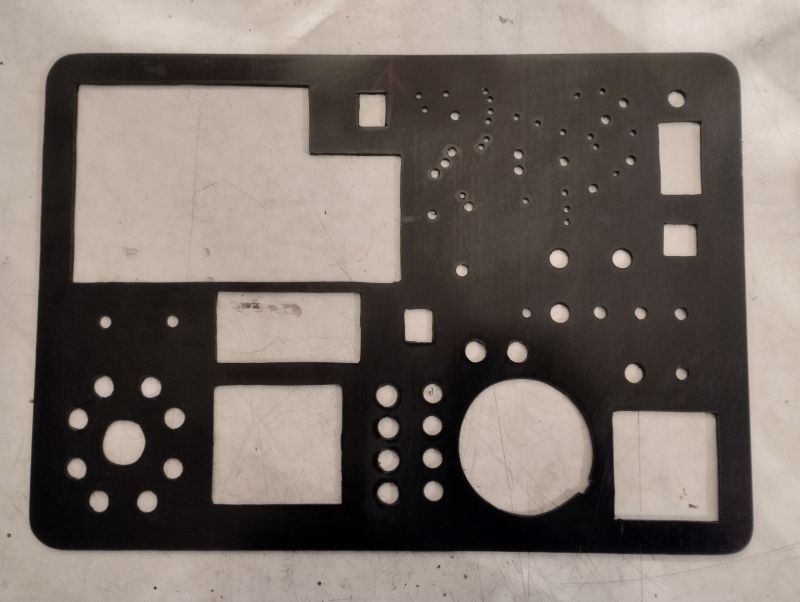 Front panel for a children's electronic console A black mounting plate with various cut-out holes and rectangular slots, prepared for installing electronic components.