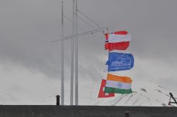 Flags at the Polish Polar Station Hornsund National flags and the flag of the Polish Polar Station Hornsund on a mast against snowy mountains and a gray sky.