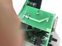 Zbliżenie na płytkę drukowaną z elementami elektronicznymi i fragmentem palca.