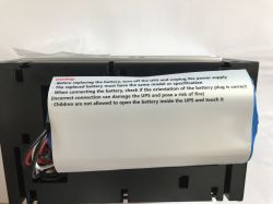 Wnętrze obudowy UPS z pakietem akumulatorów i kartką z ostrzeżeniami po angielsku