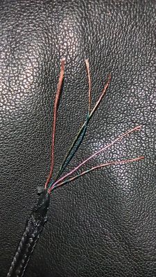 Zbliżenie na uszkodzony kabel z widocznymi odsłoniętymi miedzianymi drucikami na tle ciemnego materiału.