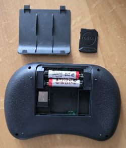 Tył bezprzewodowej klawiatury z otwartą pokrywą baterii i adapterem USB.