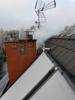 Dym lub para unosząca się z komina i odpowietrznika na ośnieżonym dachu budynku