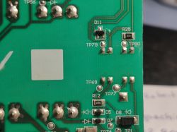 A section of a green printed circuit board with visible electronic components such as resistors and diodes, labeled with numeric symbols.