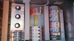 Widok wnętrza szafy sterowniczej z elementami elektrycznymi i okablowaniem.